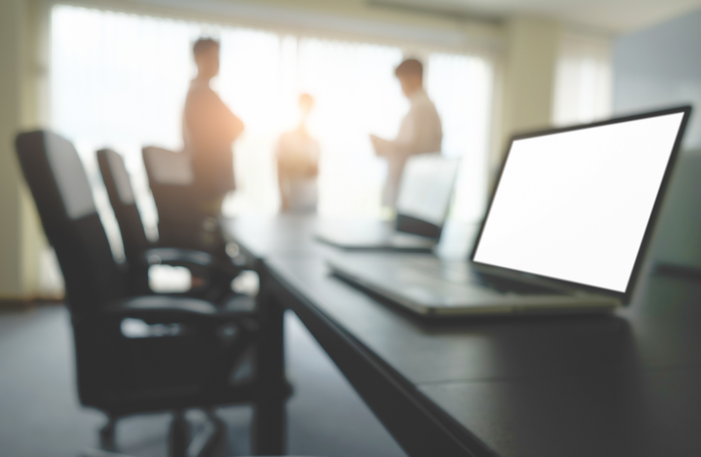 Sala de reuniones con portátiles encendidos y personas conversando al fondo de forma desenfocada