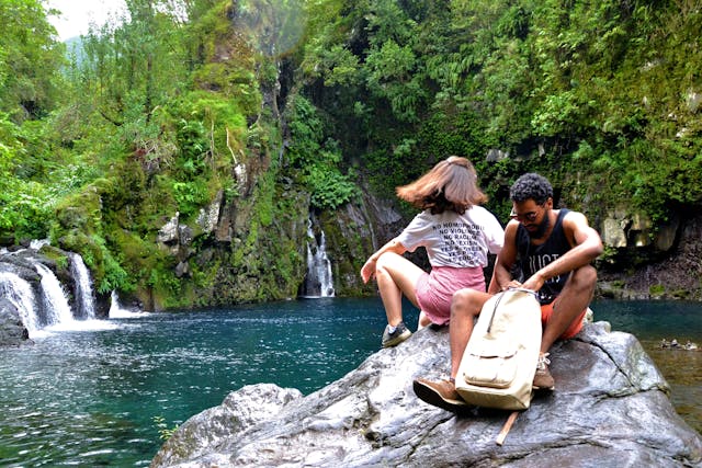 Pareja de excursionistas descansando junto a una cascada en un entorno selvático, ideal para ilustrar ecoturismo, aventura y rutas de naturaleza.