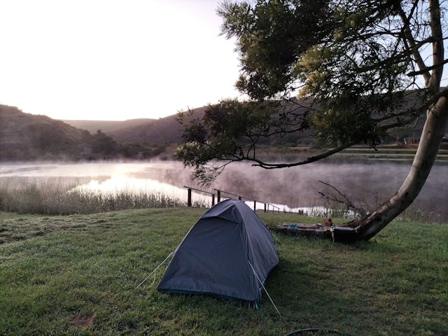 Tienda de campaña junto a un lago al amanecer con niebla, en un entorno natural y tranquilo ideal para camping, pesca y escapadas rurales.
