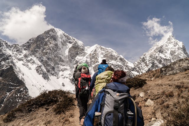 Grupo de senderistas ascendiendo por una ruta de montaña nevada en los Himalayas, ideal para ilustrar trekking, aventura y turismo de naturaleza extrema.